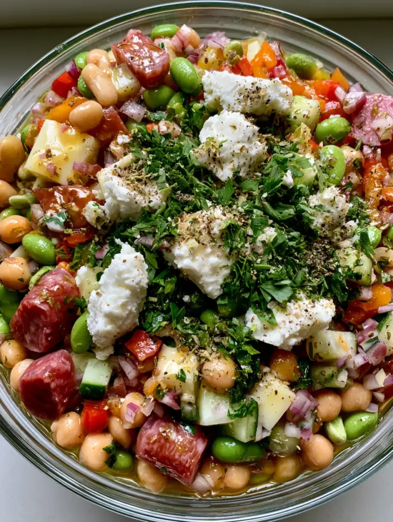 A clear glass bowl filled with a colorful mix of diced peppers, cucumbers, beans, and crumbled feta garnish.