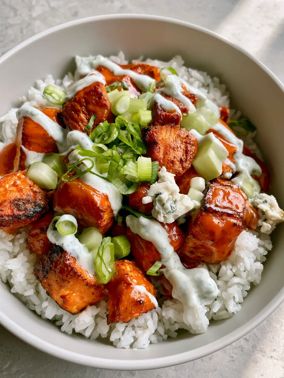 Top-down view of buffalo chicken bowls showing the glistening deep orange sauce and creamy ranch drizzle over jasmine rice.