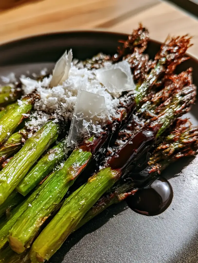 Balsamic Glazed Roasted Asparagus with Charred Tips 1 Low-angle shot of a bundle of balsamic glazed roasted asparagus topped with snow-white parmesan and Maldon sea salt flakes.