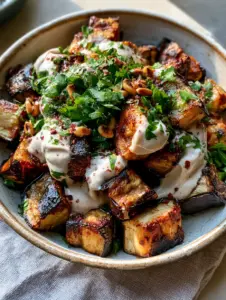 Top-down view of golden-brown roasted eggplant cubes with parsley and pine nuts in a ceramic bowl. (roasted eggplant recipe)